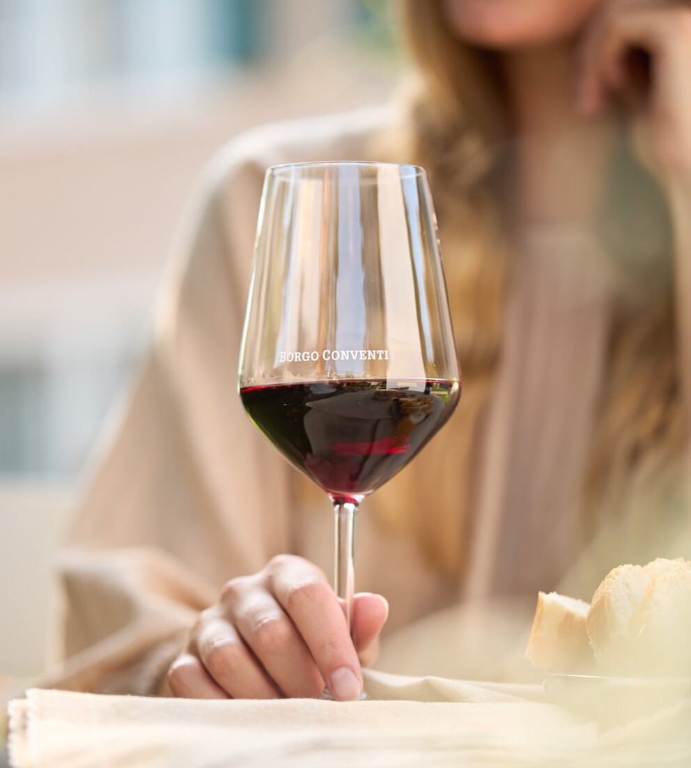 Donna seduta al tavolo con un calice di vino rosso in primo piano